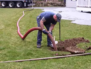 Septic pumping technician servicing a residential septic tank with a vacuum hose in Grand Rapids, MI