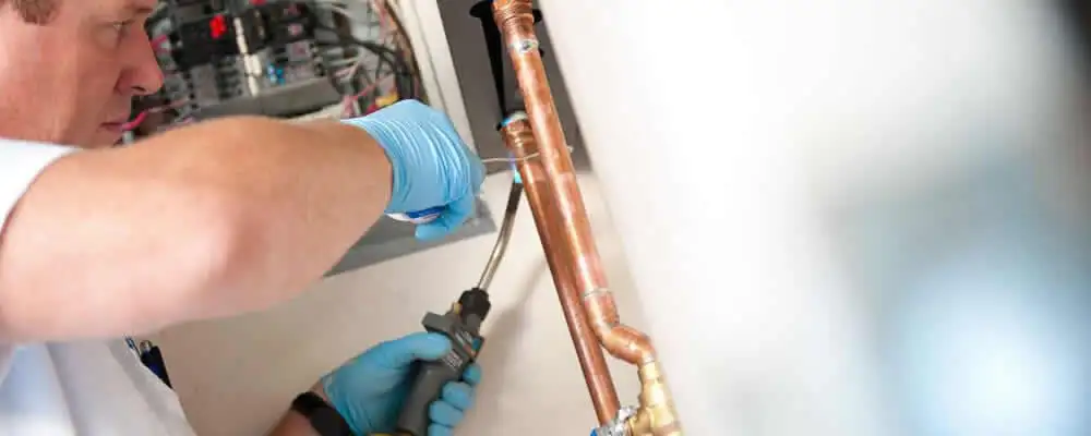 Water heater repair technician testing copper pipe connections and controls in Grand Rapids, MI